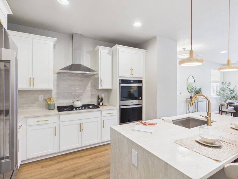 Kitchen with double wall ovens, gas cooktop, range hood, and white shaker cabinets with brass hardware