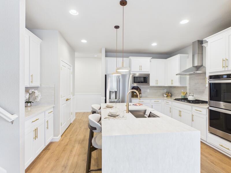 Kitchen with a large waterfall-edge island, pendant lights, white cabinets, and stainless steel appliances