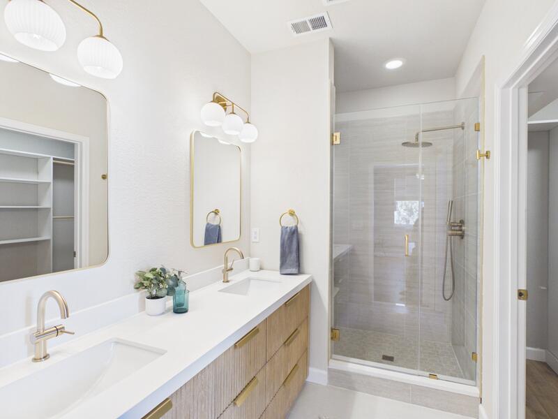 Main-level en suite bathroom with a double vanity, brass fixtures, and walk-in shower