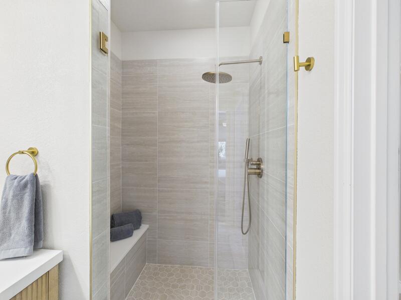 Tiled walk-in shower with glass door, rain shower head, and built-in bench