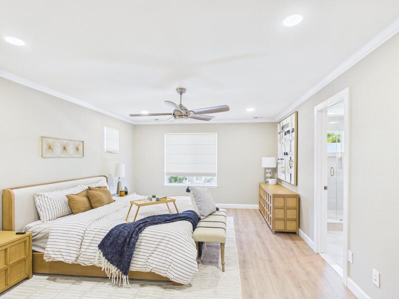 Spacious primary suite with ceiling fan, upholstered bed, and crown molding